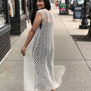 May include: A white crochet maxi dress with a loose, open-weave design. The dress is sleeveless and has a flowing silhouette.