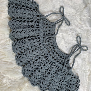 May include: A grey crocheted collar with two long ties that can be tied into bows. The collar is made with a delicate, lacy pattern.
