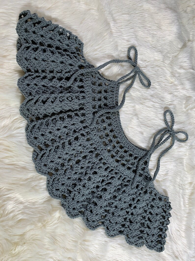 May include: A grey crocheted collar with two long ties that can be tied into bows. The collar is made with a delicate, lacy pattern.