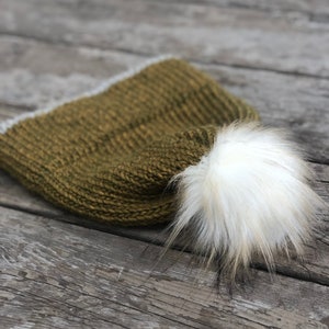 May include: A green knitted beanie with a white pom pom. The beanie has a white trim around the edge.