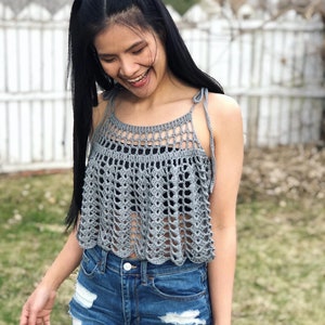 May include: A grey crochet top with a scalloped hem and thin straps. The top is worn over denim shorts.