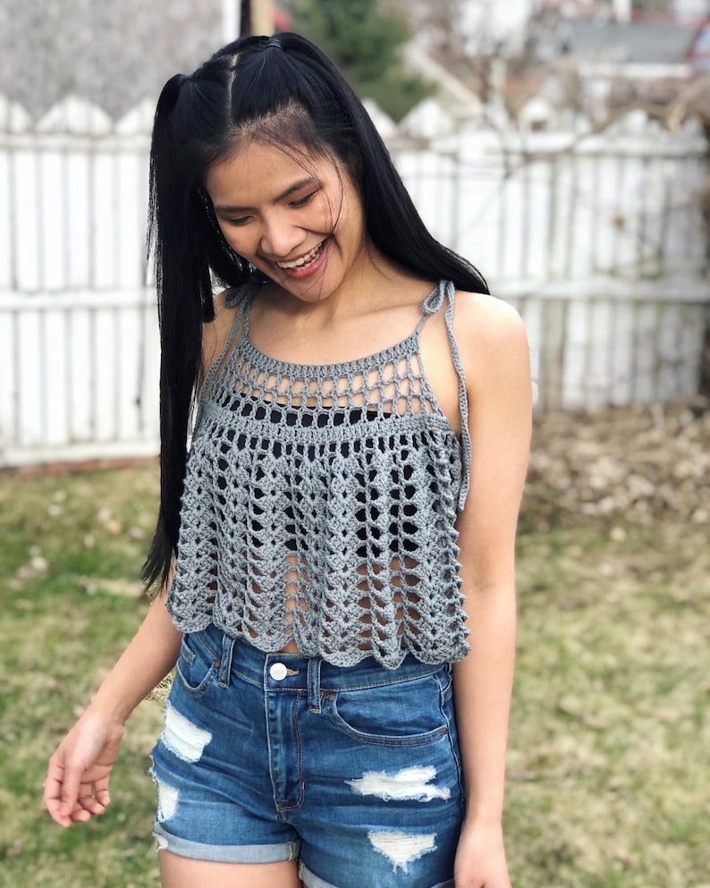 May include: A grey crochet top with a scalloped hem and thin straps. The top is worn over denim shorts.