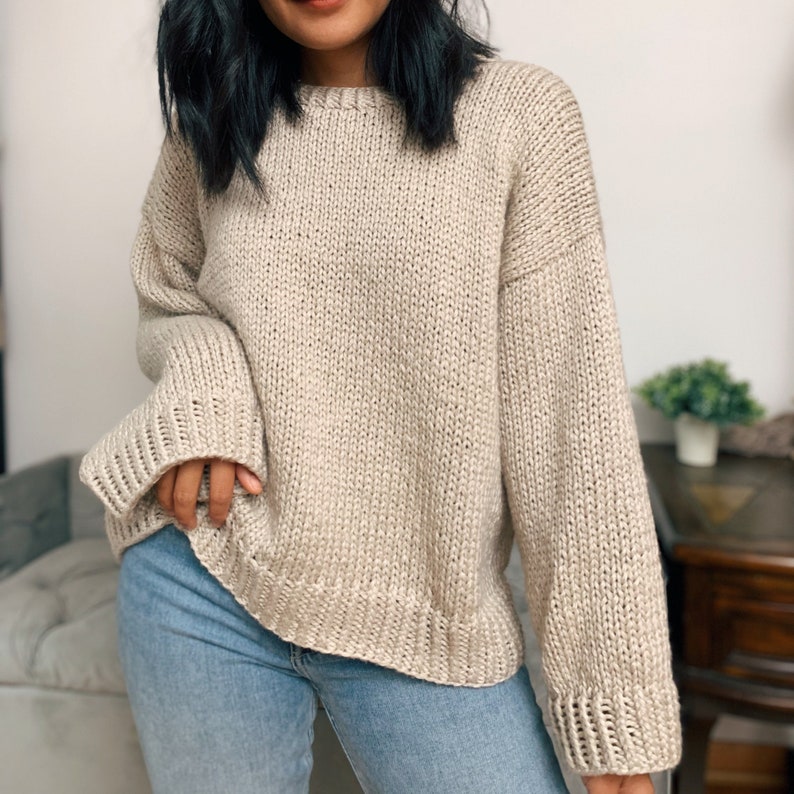 May include: A beige knitted sweater with long sleeves and a relaxed fit.