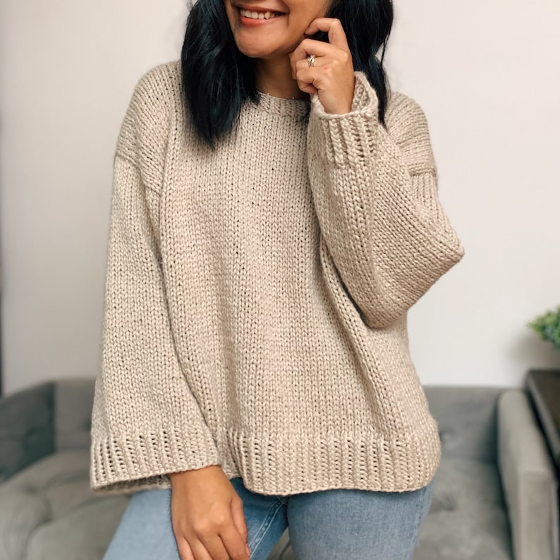 May include: A beige knitted sweater with long sleeves and a relaxed fit.