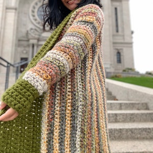 May include: A long, striped cardigan with a crocheted texture. The cardigan is made with a variety of colors, including brown, beige, and orange. The cardigan is open in the front and has long sleeves.