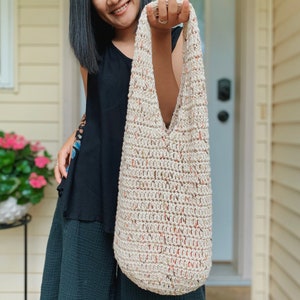 May include: A beige crocheted tote bag with a speckled pattern. The bag has a wide, open top and a single strap.