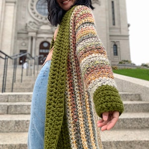 May include: A long, striped cardigan with a green crocheted trim. The cardigan is made with a variety of colors, including brown, orange, yellow, and white.