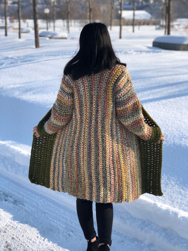 May include: A long, striped cardigan with a green trim. The cardigan is made of a soft, colorful yarn and has a relaxed fit.