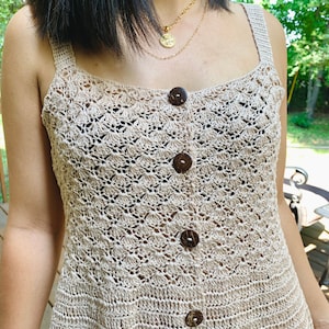 May include: A beige crochet tank top with a square neckline and coconut shell buttons. The top has a delicate, openwork design.