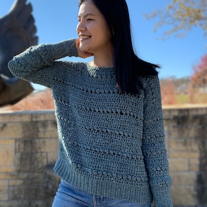 May include: A light blue crocheted sweater with a loose fit and long sleeves. The sweater has a simple, open stitch pattern.