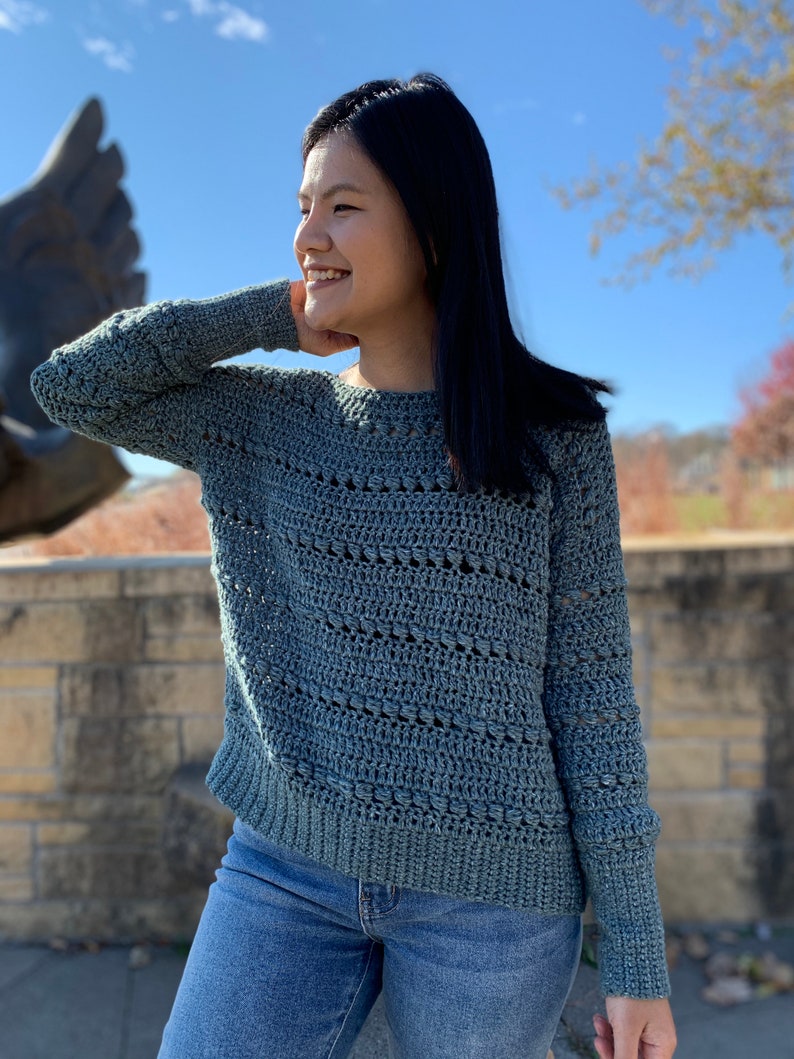 May include: A light blue crocheted sweater with a loose fit and long sleeves. The sweater has a simple, open stitch pattern.