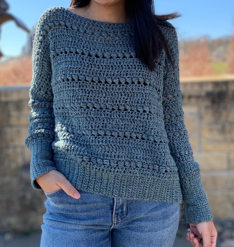 May include: A teal blue crocheted sweater with a loose fit and long sleeves. The sweater has a delicate open stitch pattern.