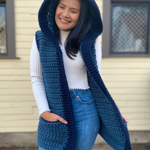 Pu&ograve; includere: Un gilet di uncinetto blu e turchese con cappuccio e tasche. Il gilet &egrave; aperto sul davanti e ha una vestibilit&agrave; rilassata.