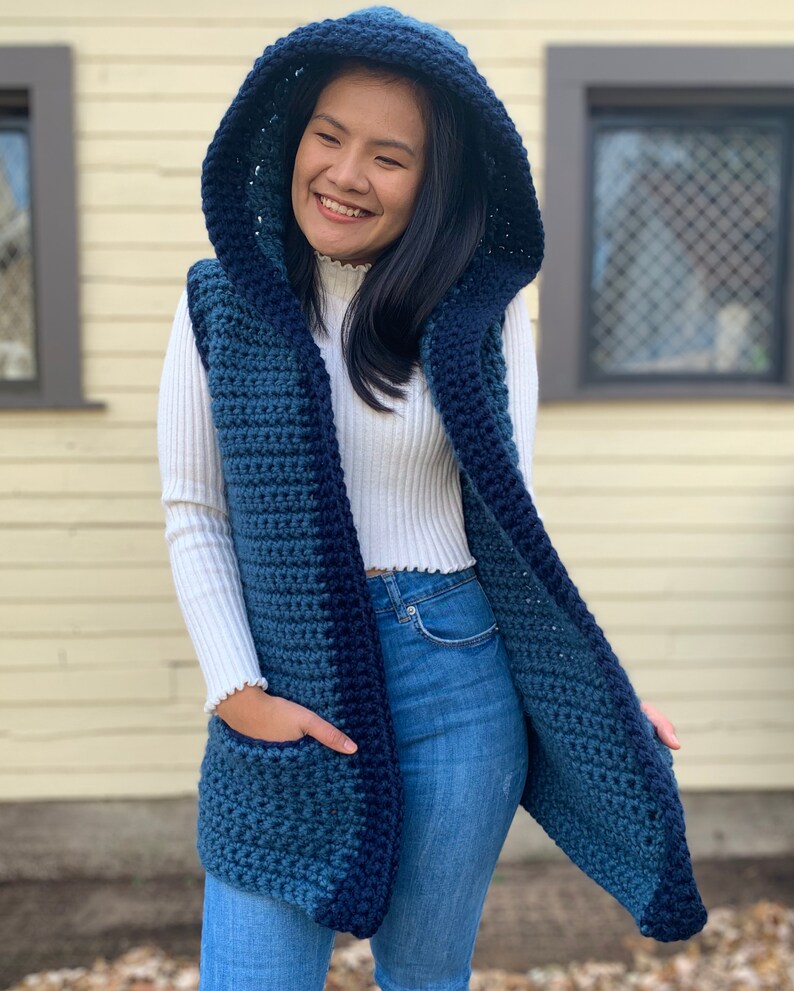 Pu&ograve; includere: Un gilet di uncinetto blu e turchese con cappuccio e tasche. Il gilet &egrave; aperto sul davanti e ha una vestibilit&agrave; rilassata.