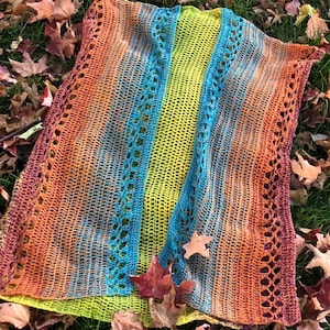 May include: A crocheted shawl with a colorful ombre design in shades of orange, blue, green, and yellow. The shawl has a lacy pattern and is made with a soft yarn.