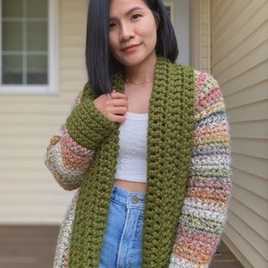May include: A long, green and multi-colored crocheted cardigan with a wide, open collar. The cardigan is worn over a white tank top and blue jeans.