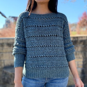 May include: A blue crocheted sweater with a loose fit and a textured pattern. The sweater has long sleeves and a round neckline.