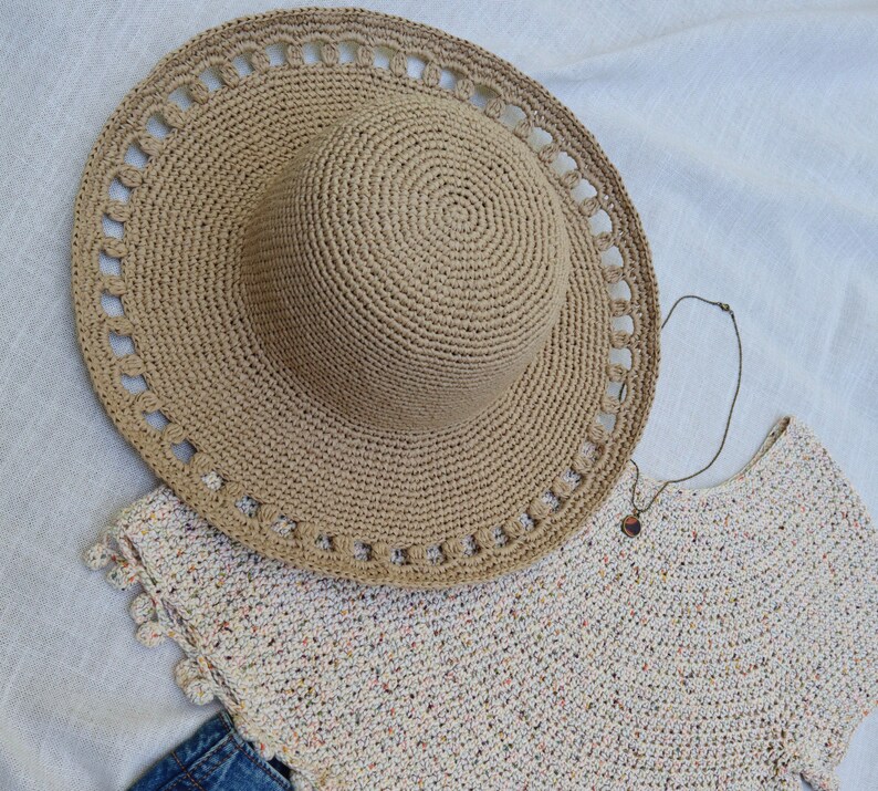 May include: A beige crochet sun hat with a wide brim and decorative cutouts, paired with a matching crochet top and a necklace. The hat's brim measures approximately 15 inches in diameter. The top has a speckled pattern.
