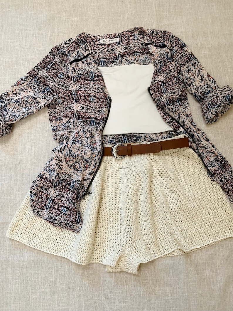 Puede incluir: Una falda de crochet blanca con un cintur&oacute;n marr&oacute;n, un top blanco y una camisa estampada en blanco y negro.