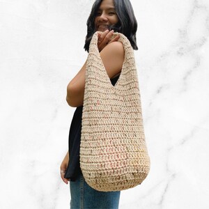 May include: A beige crocheted tote bag with a speckled pattern. The bag has a wide, open top and a long strap.