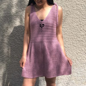 May include: A sleeveless, light purple crochet dress with a V-neck and a bow detail at the neckline.