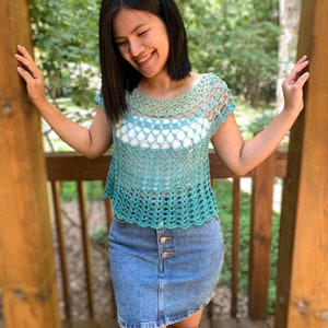 Op de afbeelding: Een gecrochet top met een groene en witte ombre-kleur. De top heeft een ronde hals en korte mouwen. De top is gemaakt met een delicaat open steekpatroon.