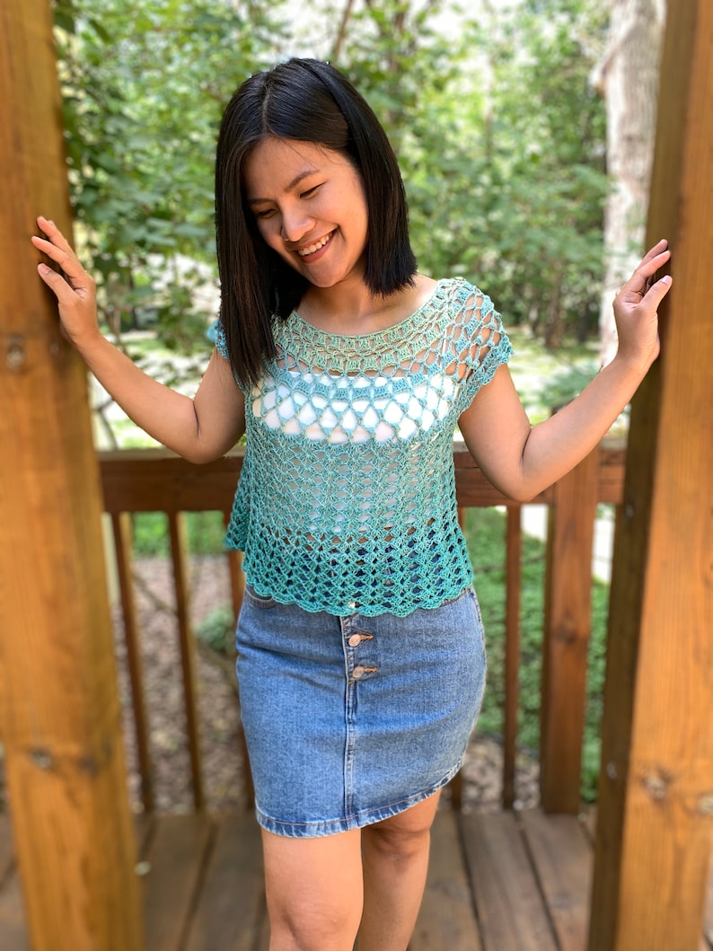 Op de afbeelding: Een gecrochet top met een groene en witte ombre-kleur. De top heeft een ronde hals en korte mouwen. De top is gemaakt met een delicaat open steekpatroon.