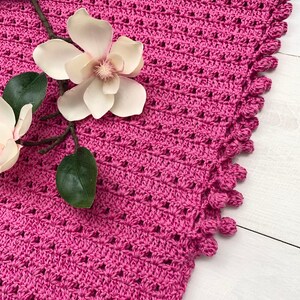 May include: A pink crocheted shawl with a scalloped edge and a delicate floral pattern. The shawl is made with a soft yarn and has a lightweight feel.