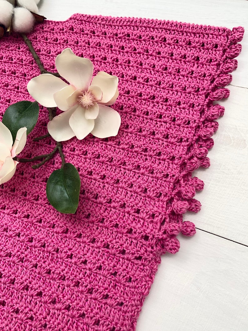 May include: A pink crocheted shawl with a scalloped edge and a delicate floral pattern. The shawl is made with a soft yarn and has a lightweight feel.
