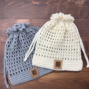 Pode incluir: Duas bolsas de malha de crochê com cordões, uma cinza e outra branca, com uma etiqueta de couro marrom que diz "KnitAddict" em cada uma.