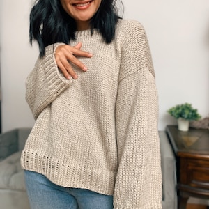 May include: A beige knitted sweater with long sleeves and a relaxed fit.