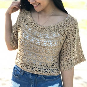 Peut inclure: Haut en crochet beige avec un col en V et des manches courtes évasées. Le motif ajouré révèle un sous-vêtement blanc. Le haut est associé à un short en jean bleu, créant un look décontracté et estival.