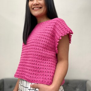 May include: A pink crochet top with short sleeves and a scalloped edge. The top has a loose fit and a round neckline.