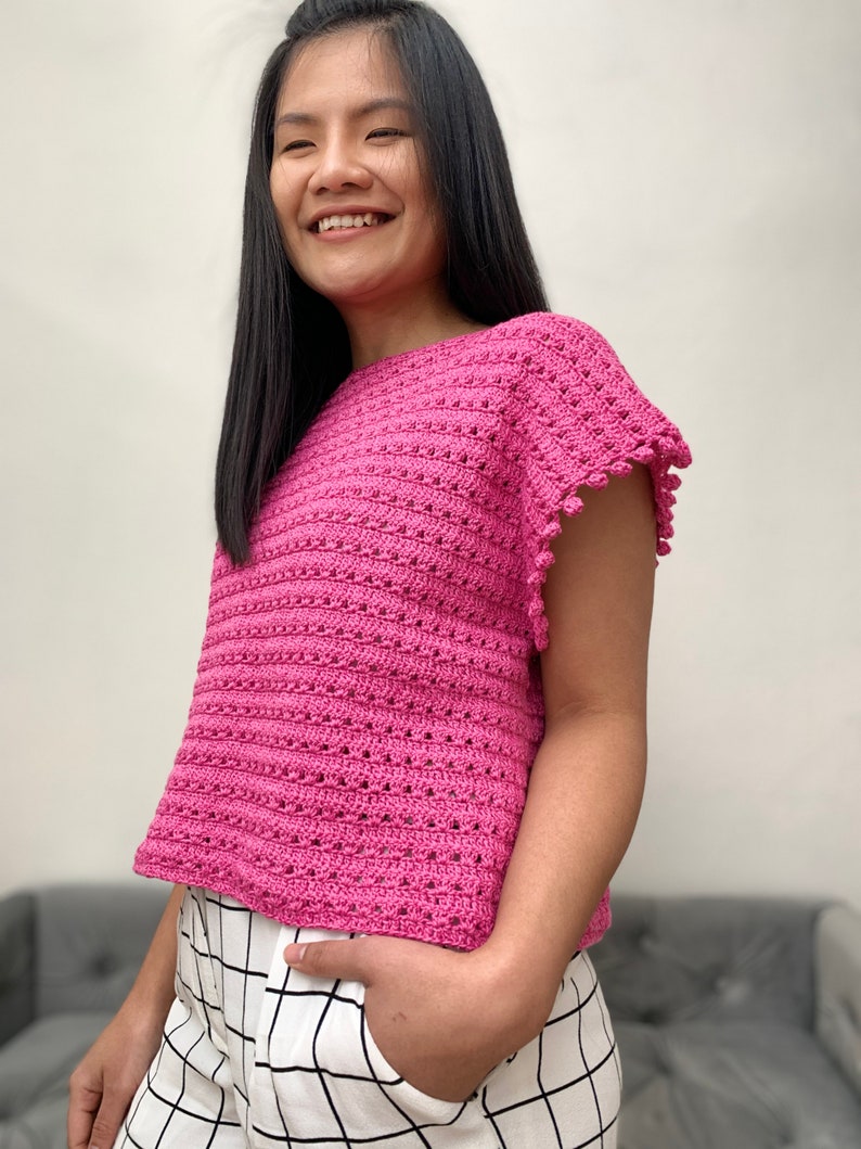 May include: A pink crochet top with short sleeves and a scalloped edge. The top has a loose fit and a round neckline.