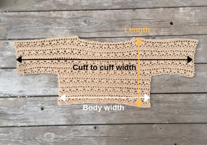 Puede incluir: Un top de ganchillo beige de tejido abierto, colocado plano sobre una superficie de madera. El top se mide con l&iacute;neas negras y amarillas que indican la longitud, el ancho de pu&ntilde;o a pu&ntilde;o y el ancho del cuerpo. El dise&ntilde;o de ganchillo presenta un patr&oacute;n delicado y aireado.