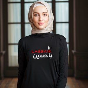 Pode incluir: Camiseta preta de manga comprida com uma estampa gráfica branca que diz "Labbaik Ya Hussein" em escrita árabe. O gráfico também inclui um punho levantado.