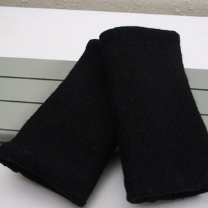 Könnte beinhalten: Zwei schwarze Armstulpen aus Stoff, gefaltet und auf einer weißen Oberfläche liegend. Die Armstulpen bestehen aus einem weichen, strukturierten Material. Der Hintergrund enthält ein graues Element mit horizontalen Linien.