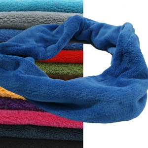 Könnte beinhalten: Ein blaues Fleece-Stirnband mit weicher, plüschiger Textur ist das Hauptmotiv. Das Stirnband ist geschlungen und verdreht. Im Hintergrund ist ein Stapel farbiger Fleece-Stoffe in verschiedenen Farben, darunter Türkis, Grau, Rot und Lila, zu sehen.