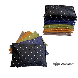 Könnte beinhalten: Ein Stapel von acht rechteckigen Kissen mit einem weißen Sternenmuster auf verschiedenen farbigen Stoffen, darunter Schwarz, Marineblau, Grün, Orange und Braun. Die Kissen sind in einem Stapel angeordnet, wobei das schwarze Kissen oben liegt. Die Kissen sind alle gleich groß und gleich geformt.