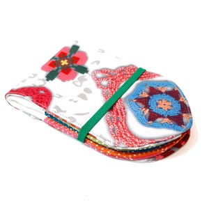 Könnte beinhalten: Ein weißes Stoffetui mit einem bunten Häkelmuster. Das Etui hat ein grünes Gummiband und ist gefaltet, um die verschiedenen Stoffschichten zu zeigen.