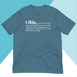 Peut inclure: Un t-shirt bleu sarcelle avec le mot "Uffda" en texte blanc. Le mot est défini comme une interjection en norvégien, signifiant une expression de confusion, de surprise, de soulagement, d'épuisement, de découragement, de déception ou un choc soudain aux sens ; souvent un marqueur de l'héritage scandinave.