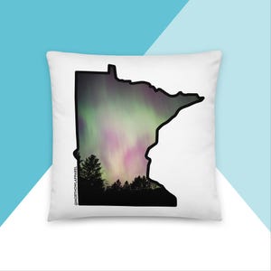 Puede incluir: Almohada blanca con un contorno negro del estado de Minnesota relleno con una imagen colorida de aurora boreal. El texto "@northhowlapparel" está en la esquina inferior izquierda de la almohada.