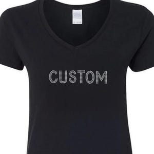 Könnte beinhalten: Schwarzes V-Ausschnitt-T-Shirt mit dem Wort "CUSTOM" in Strasssteinen auf der Brust. Das kurzärmlige Shirt hat eine klassische Passform und ist für den Freizeitgebrauch geeignet.