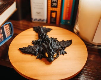 May include: A black dragon figurine with gold eyes, sitting on a wooden coaster.