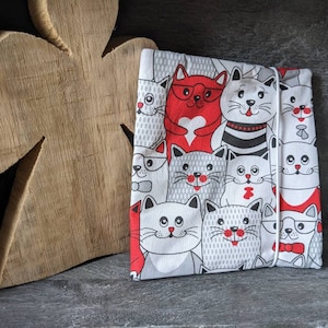 Könnte beinhalten: Eine weiße Stofftasche mit Kordelzug zeigt ein Muster aus Comic-Katzen mit roten, schwarzen und weißen Akzenten. Die Katzen tragen Brillen, Fliegen und andere Accessoires.