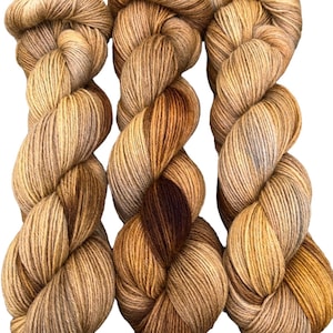 Könnte beinhalten: Drei Knäuel Garn in Braun-, Beige- und Grautönen. Das Garn ist mehrfarbig, die Farben verschmelzen sanft miteinander.