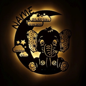 May include: A black silhouette of an elephant with a crescent moon behind it. The elephant is sitting with its legs crossed. The moon has stars and clouds around it. The text on the moon reads "NAME 21:35 Uhr 12.08.2019 3120g 52cm".