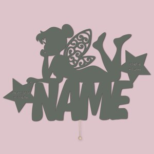 May include: A green wooden fairy silhouette with wings and a star, with the name "NAME" written below. The fairy is lying on her side, with her head resting on her hand. The star has the words "Do you believe in fairy dust?" written on it.