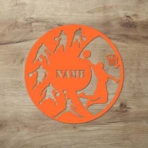 May include: Orange basketball themed wall clock with silhouettes of basketball players and a basketball hoop. The clock face has a space for a name, "NAME".