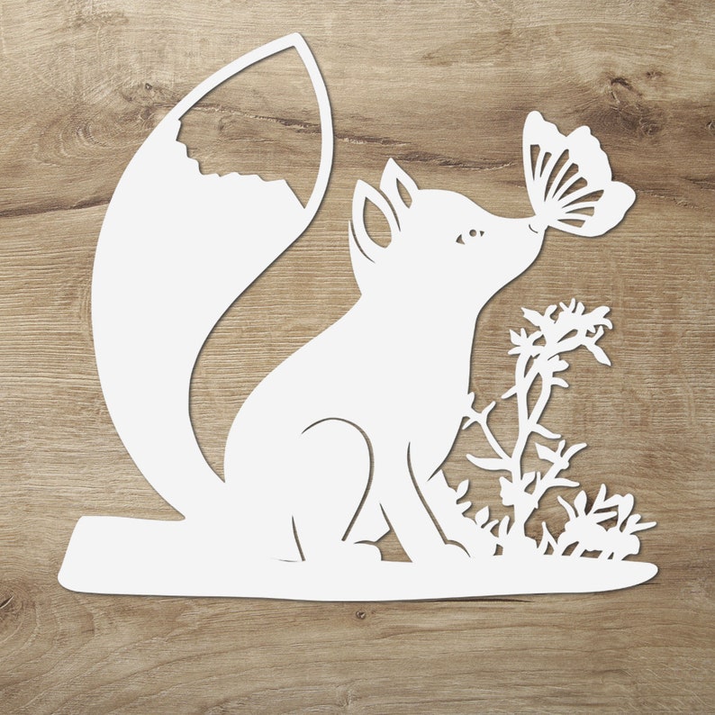 May include: White paper cut-out of a fox with a butterfly on its nose. The fox is sitting on a branch with a small bush behind it.